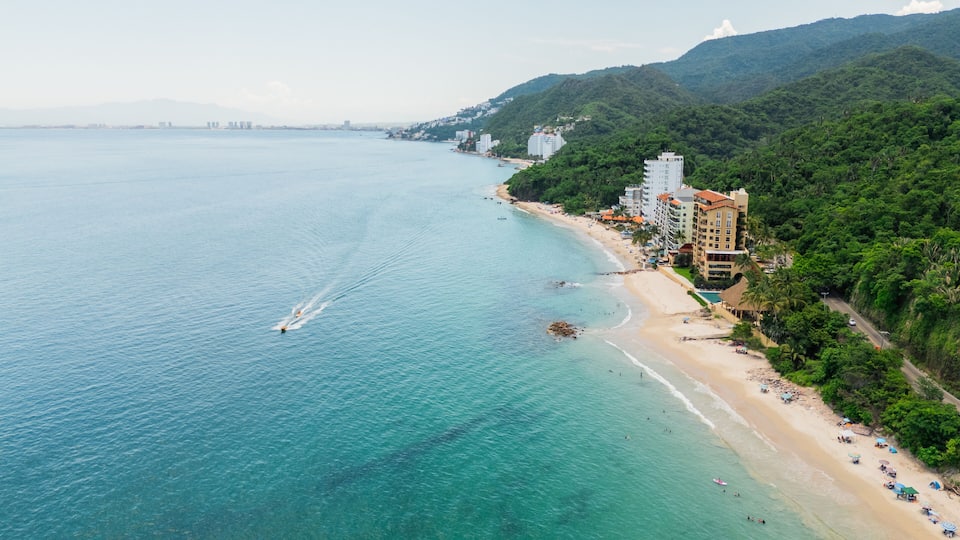 A coastal city with a beach, buildings, and a mountainous backdrop.
