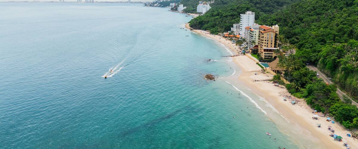 A coastal city with a beach, buildings, and a mountainous backdrop.