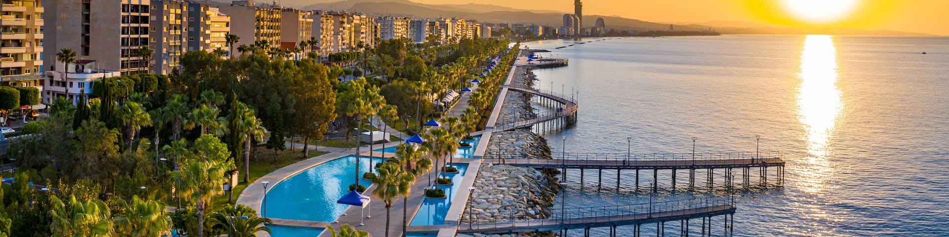 A waterfront resort with a swimming pool, palm trees, and a pier extending into the water.