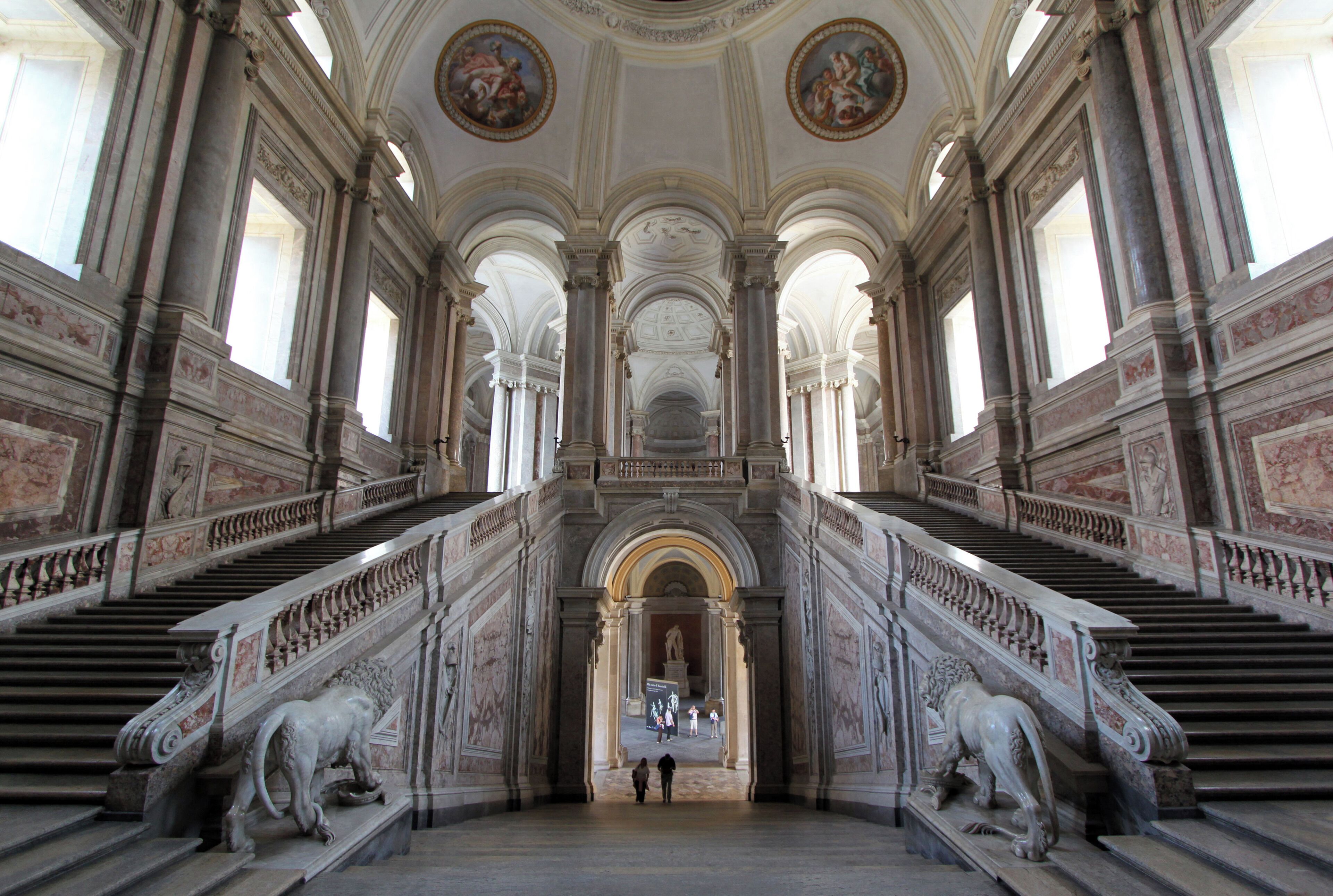 Una imponente escalera con barandales ornamentados y estatuas de leones, que conduce a un arco central.