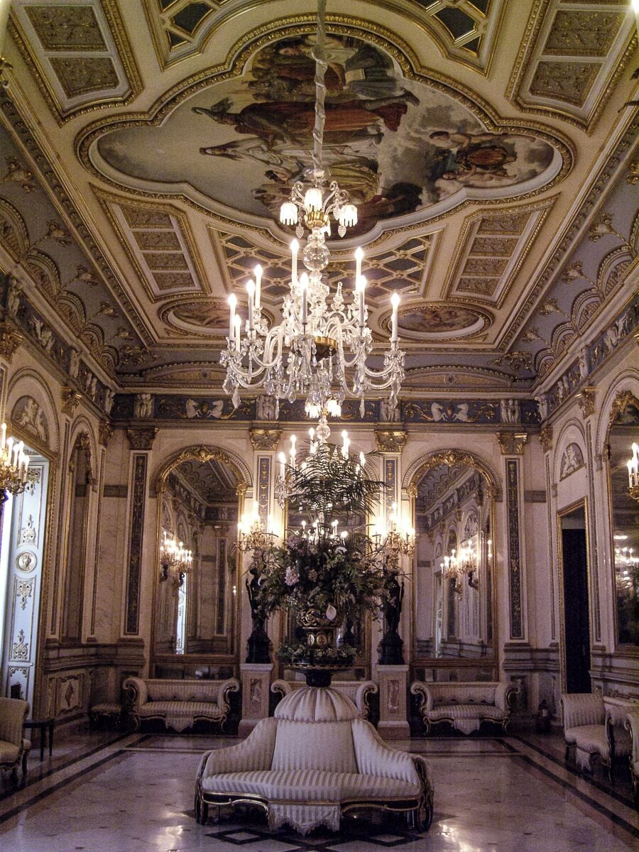 Une pièce somptueuse, ornée d’un magnifique lustre, d’un plafond richement décoré et présentant une architecture classique.