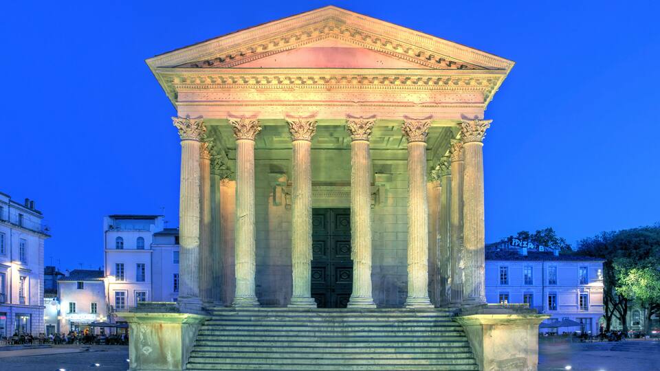A classical neoclassical building with columns and a pediment, illuminated at dusk.