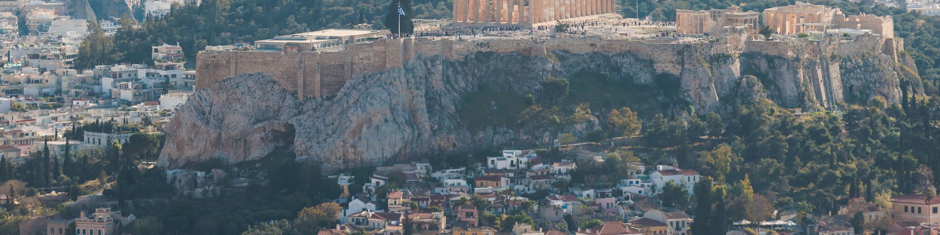The Acropolis of Athens with the Parthenon on top, surrounded by the cityscape and the Aegean Sea in the background.