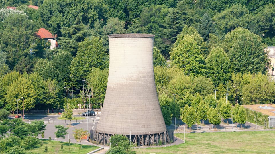 A large cooling tower surrounded by trees and a parking lot.