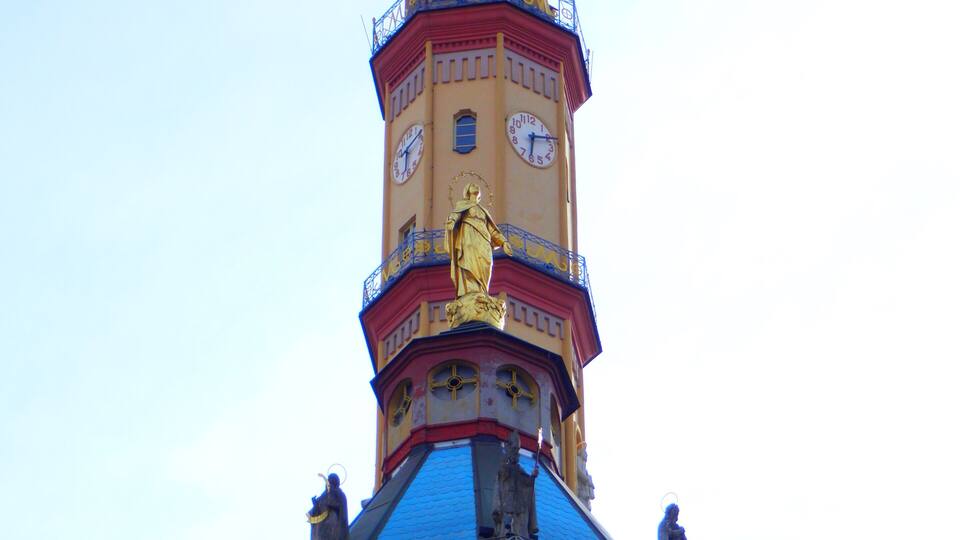 A tower with a golden statue on top, a clock, and a blue roof.