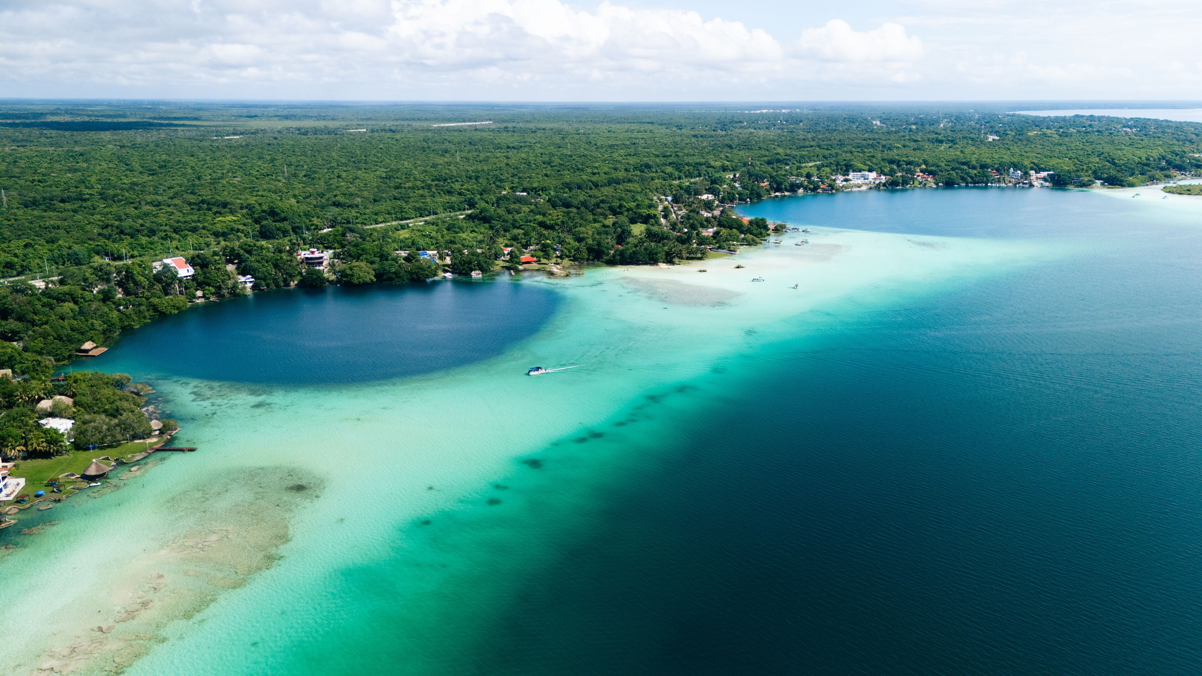 Aerial view of the contrasting turquoise waters meeting the deep blue sinkhole, surrounded by verdant foliage, Bacalar, Mexico.