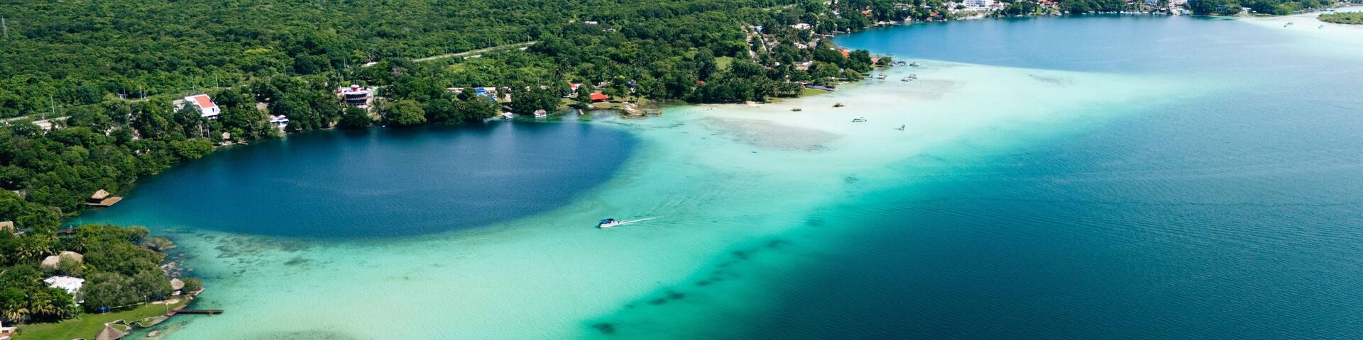 Aerial view of the contrasting turquoise waters meeting the deep blue sinkhole, surrounded by verdant foliage, Bacalar, Mexico.