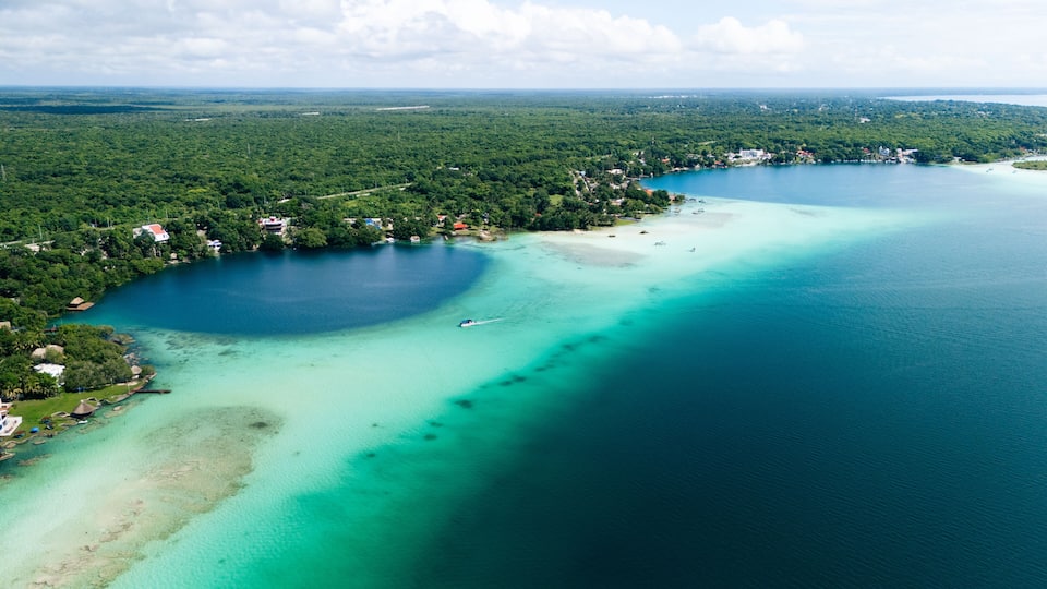 Aerial view of the contrasting turquoise waters meeting the deep blue sinkhole, surrounded by verdant foliage, Bacalar, Mexico.