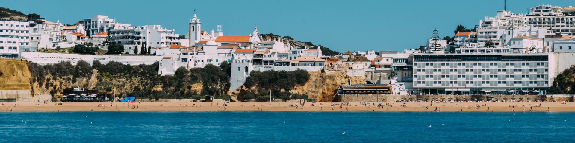 A coastal town with white buildings, a lighthouse, and a beach.