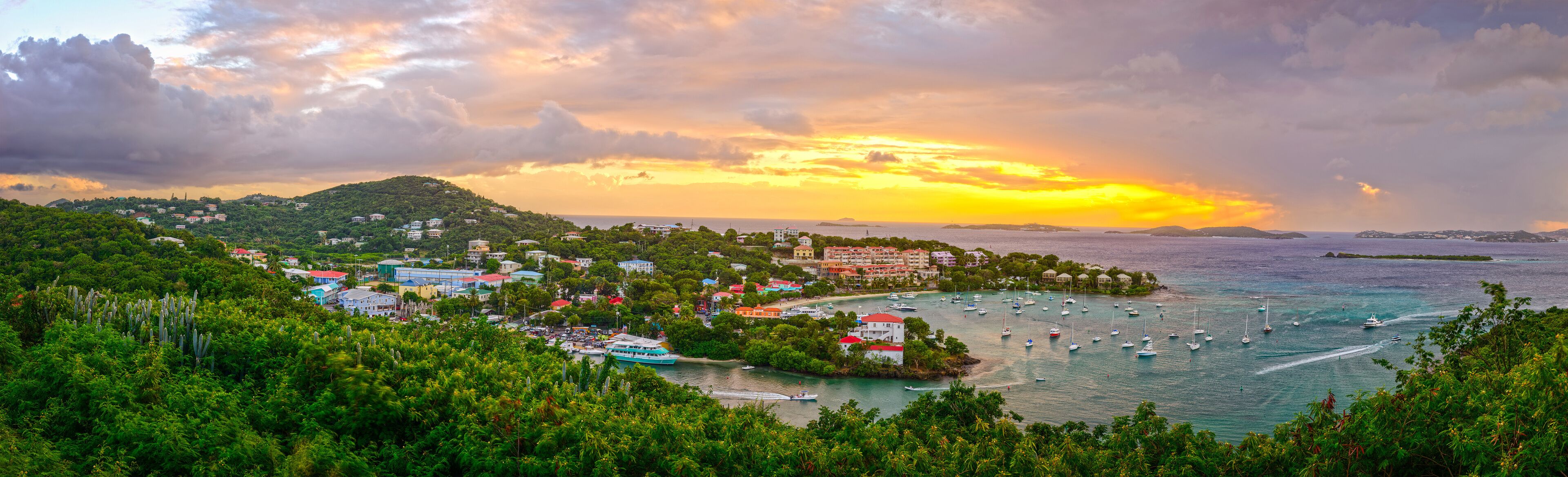 A coastal town with a marina, lush greenery, and a sunset over the ocean.