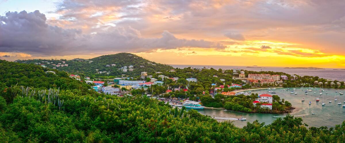 A coastal town with a marina, lush greenery, and a sunset over the ocean.