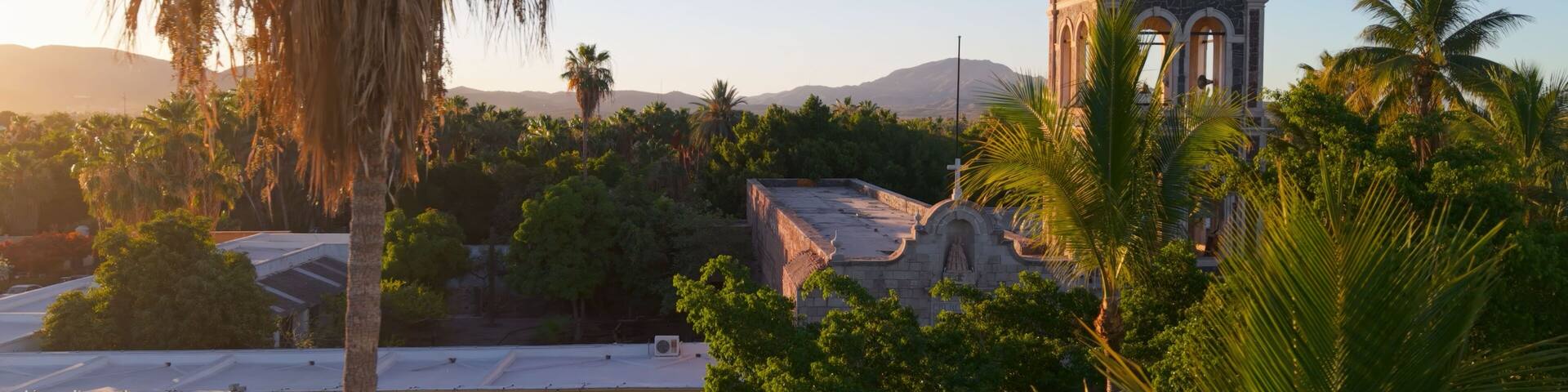 Sunset warms Loreto Mission church in Baja California Sur, Mexico, with palm trees framing its historical beauty