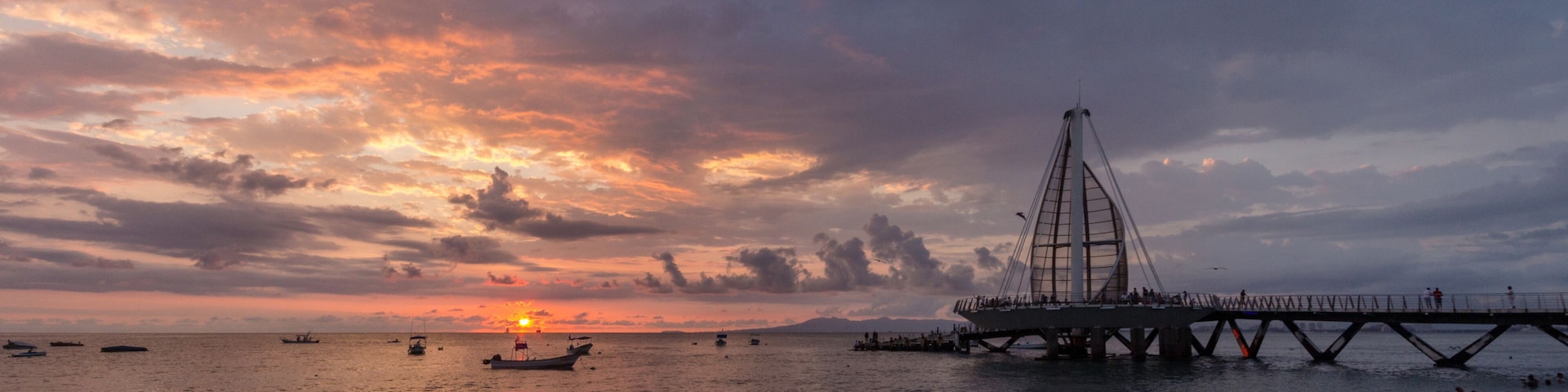 Ein Sonnenuntergang über dem Meer mit einer Brücke und Booten.