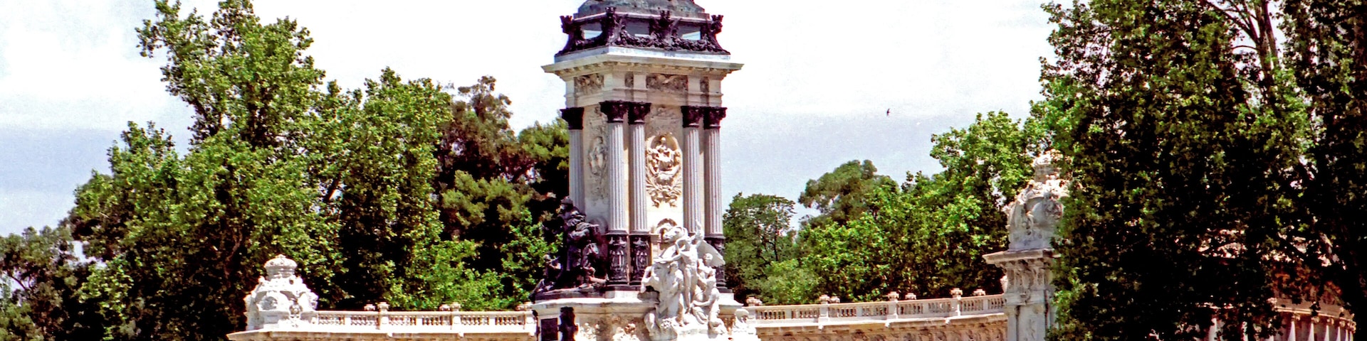 Una gran fuente con una estatua de un hombre a caballo, rodeada de columnas y estatuas, con barcos en el agua al frente.