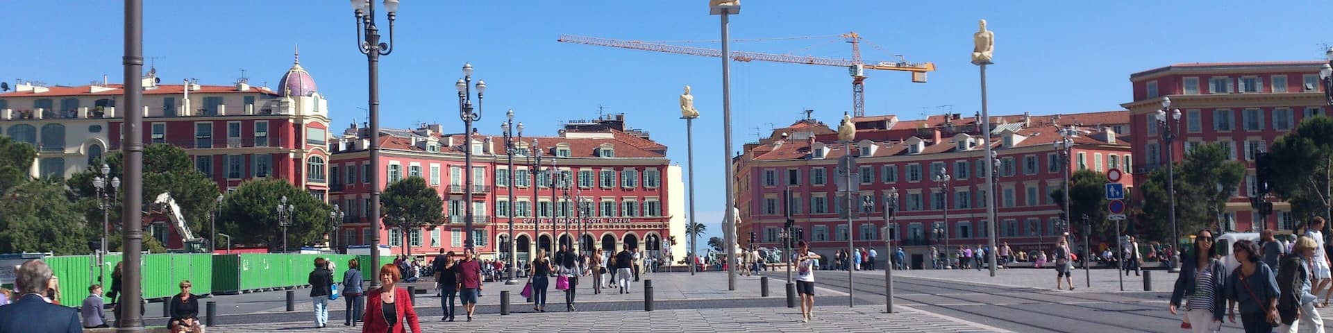 A plaza with a checkered floor, people walking, and historic buildings in the background.