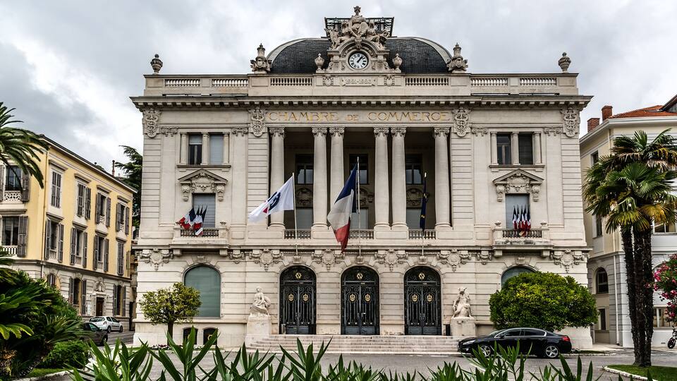 A historic building with columns and flags, featuring a dome and statues.