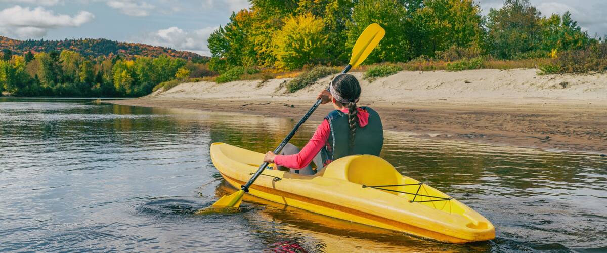 A person kayaking on a river with a forested hillside in the background.