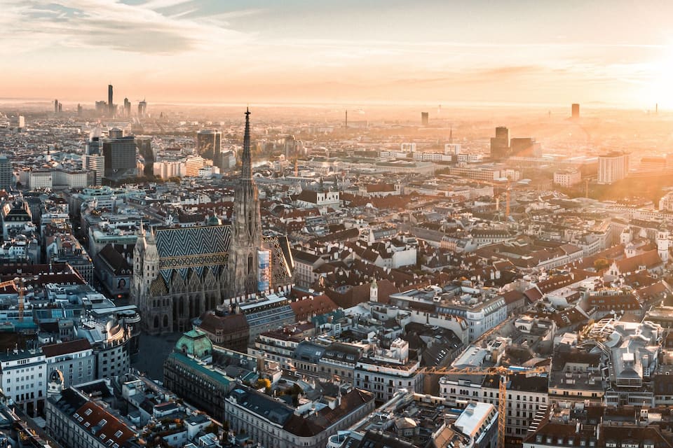 A panoramic view of a cityscape with a prominent cathedral and modern skyscrapers during sunset.