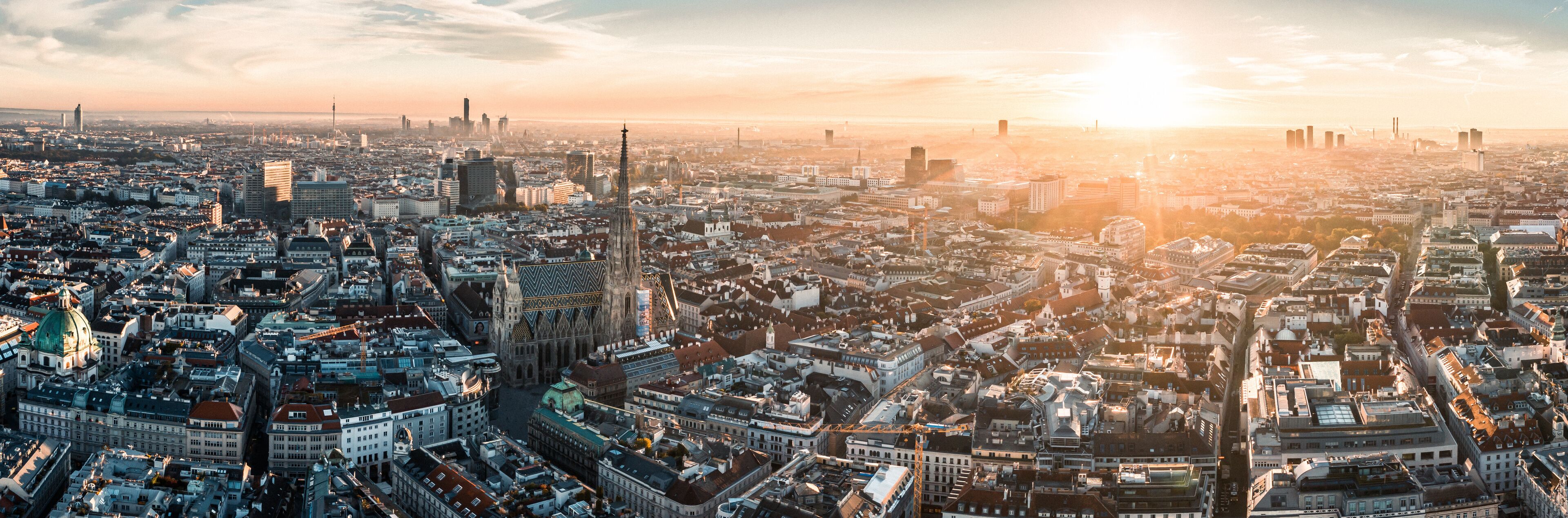 A panoramic view of a cityscape with a prominent cathedral and modern skyscrapers during sunset.