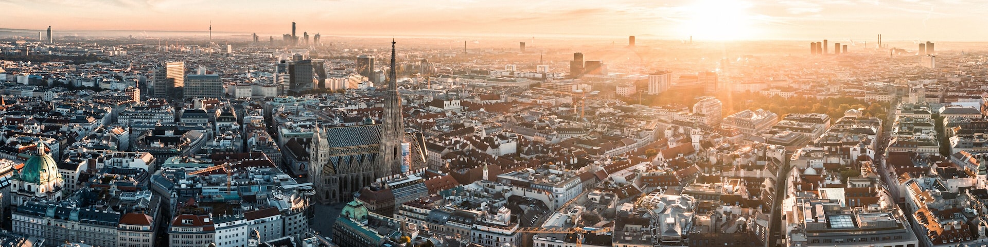 A panoramic view of a cityscape with a prominent cathedral and modern skyscrapers during sunset.