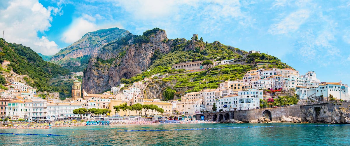 A coastal town with colorful buildings, a beach, and a mountainous backdrop.