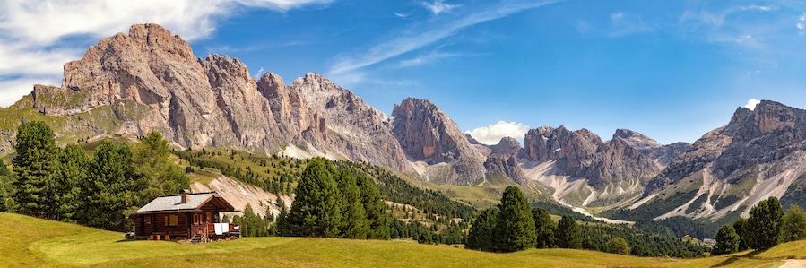 Una baita di legno in un paesaggio montuoso, con cime scoscese e fitte foreste.