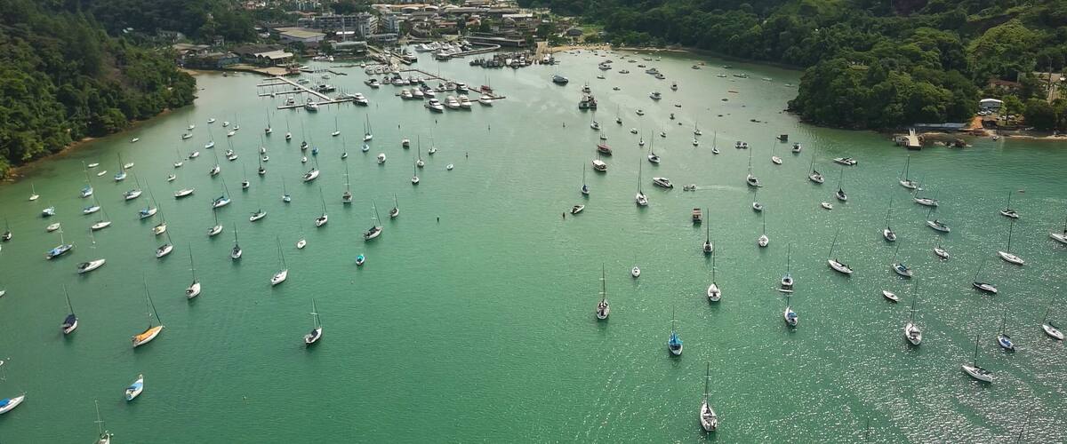 A marina filled with sailboats surrounded by lush green hills and a distant lake.