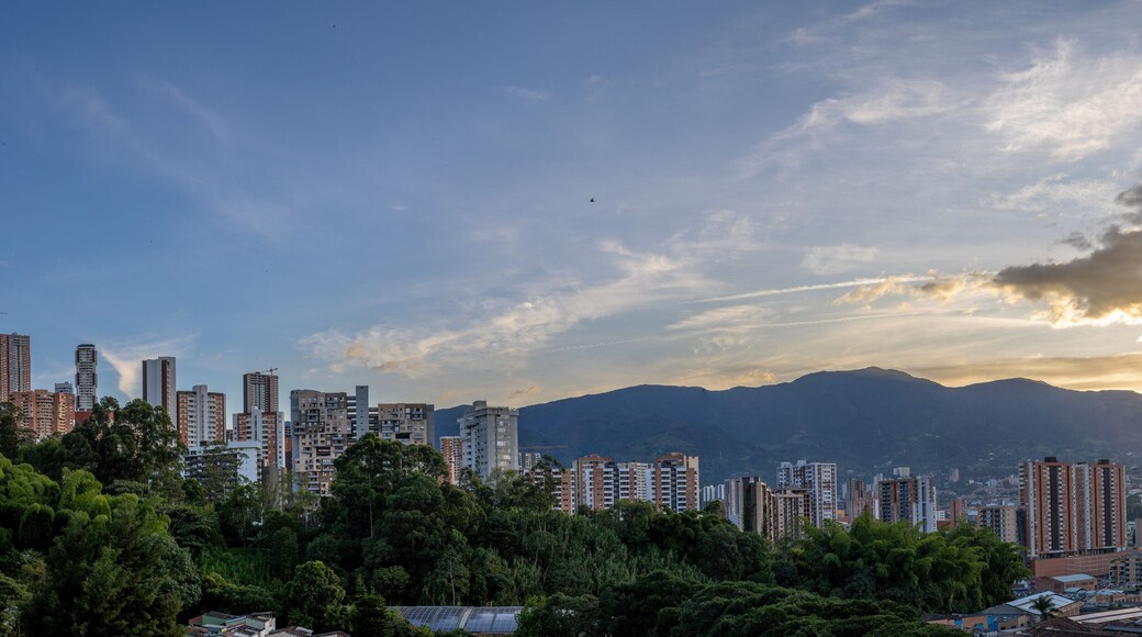Panoramic sunset over Medellín, Colombia, with city buildings silhouetted against colorful clouds and mountain backdrop. A vibrant urban scene capturing the beauty of twilight.