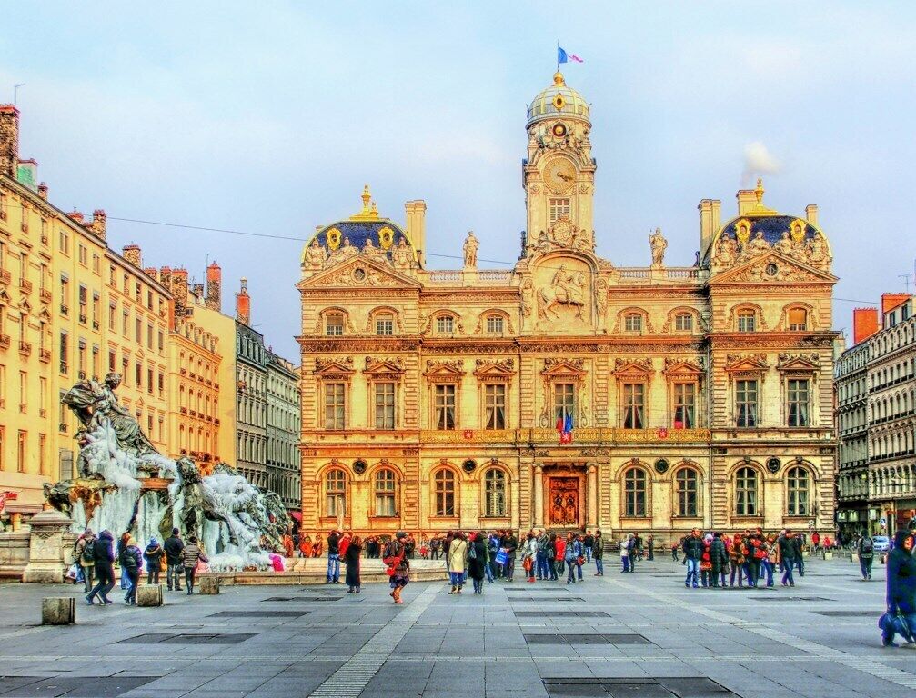 Un edifici històric amb arquitectura ornamentada, una torre del rellotge destacada i una font gran al primer pla.
