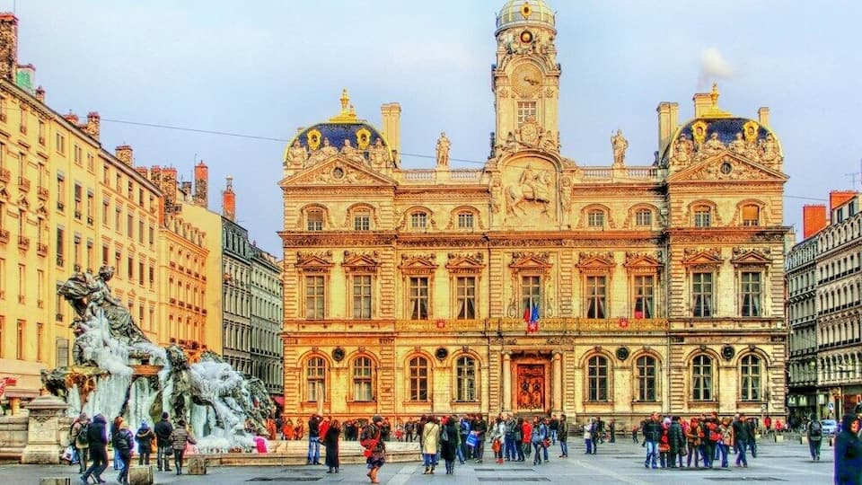 Un edifici històric amb arquitectura ornamentada, una torre del rellotge destacada i una font gran al primer pla.