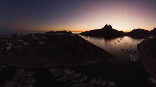 Un paisaje costero con un puerto deportivo, barcos y una montaña destacada al atardecer.