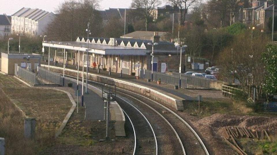 Une gare avec des voies ferrées, un quai et des bâtiments environnants.