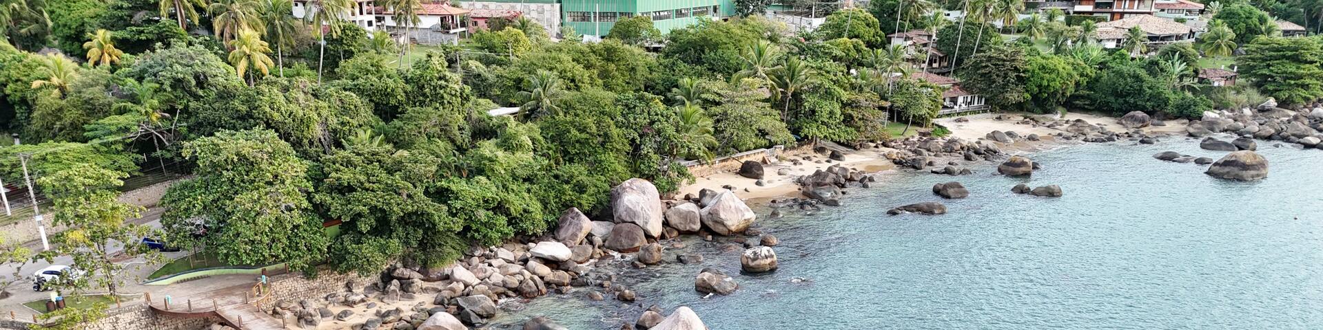 A coastal area with a wooden pier extending into turquoise waters, surrounded by lush greenery and rocky shores.
