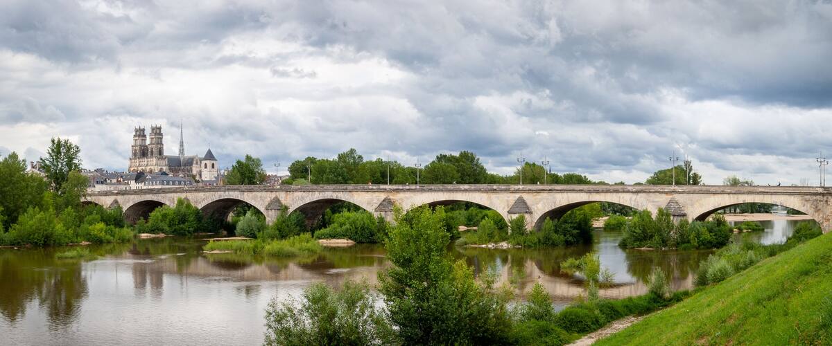 A stone bridge over a river with lush greenery and a historic building in the background.