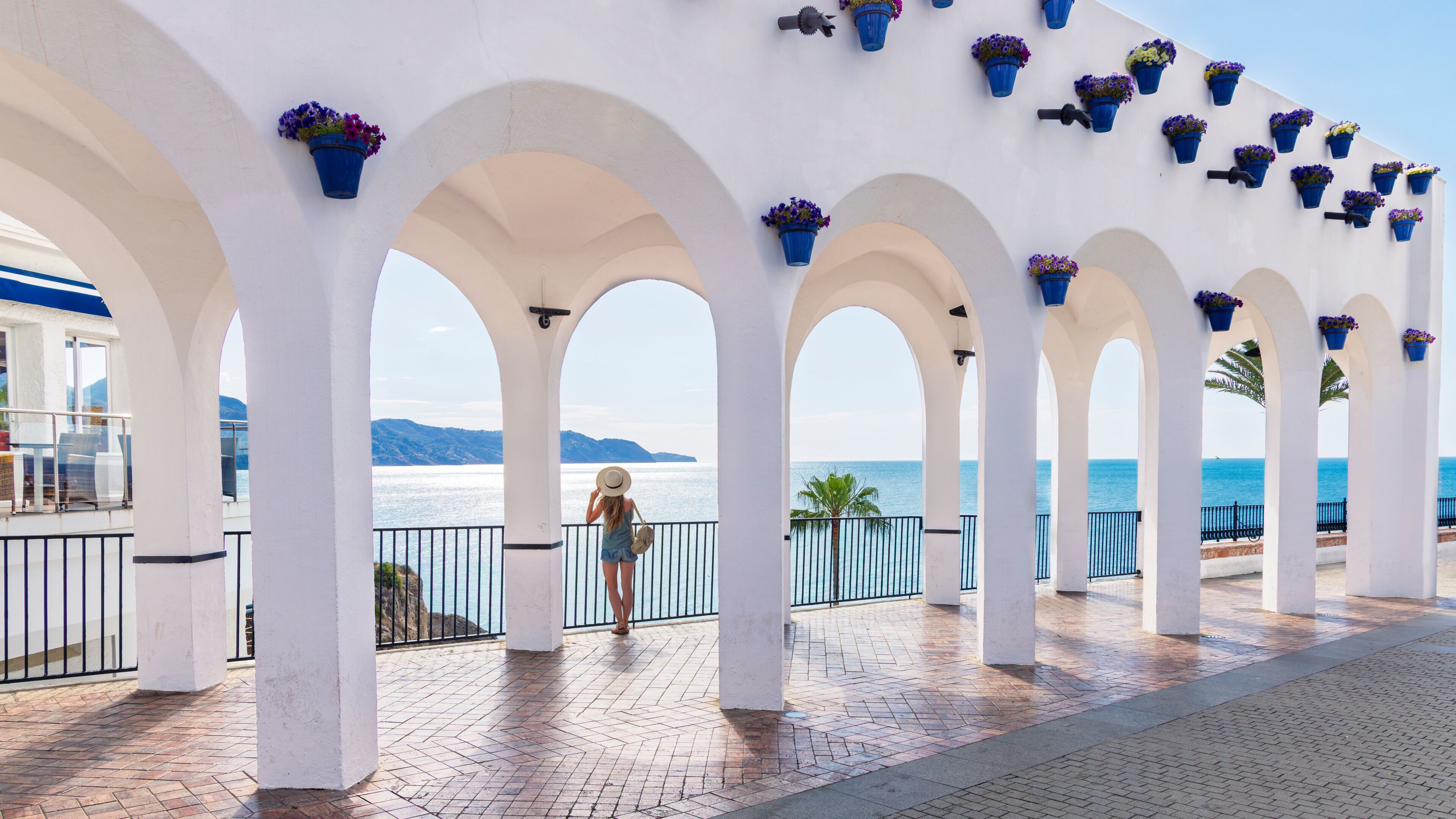 balcon de europa in nerja, andalusia, spain, white arches with blue flower pots overlooking the mediterranean sea and a woman traveler