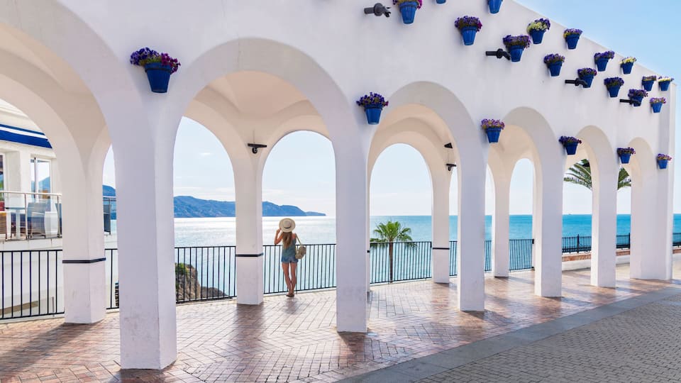 balcon de europa in nerja, andalusia, spain, white arches with blue flower pots overlooking the mediterranean sea and a woman traveler