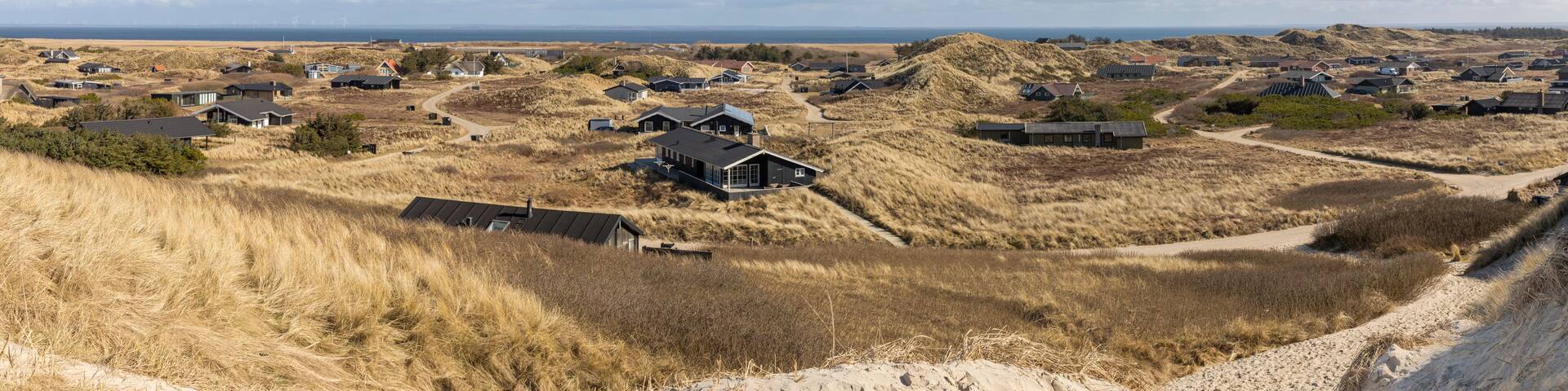 A coastal settlement with houses on dunes, a clear sky, and a distant view of the sea.