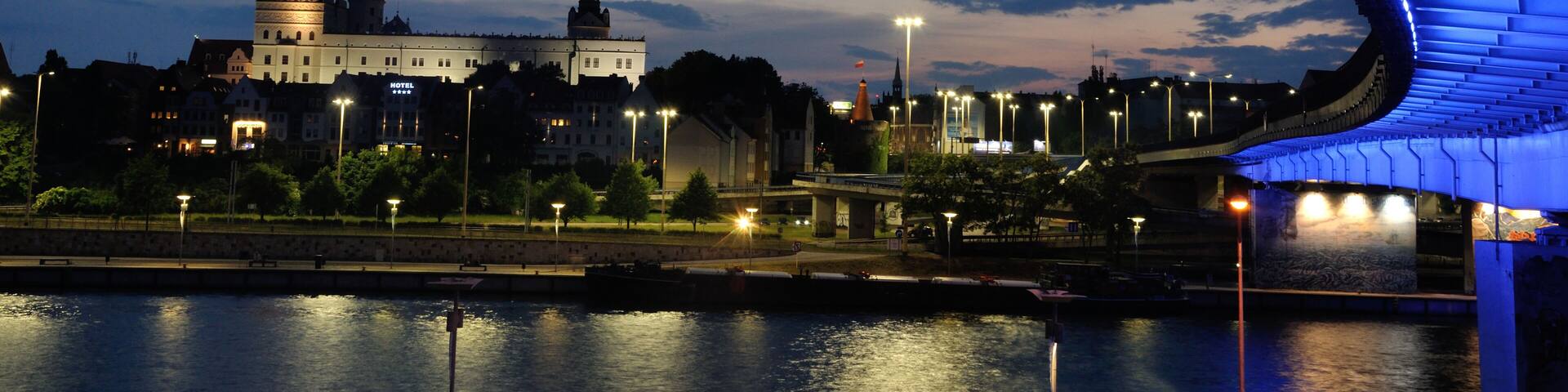 A river with a bridge, a castle-like building, and a modern bridge with blue lighting.