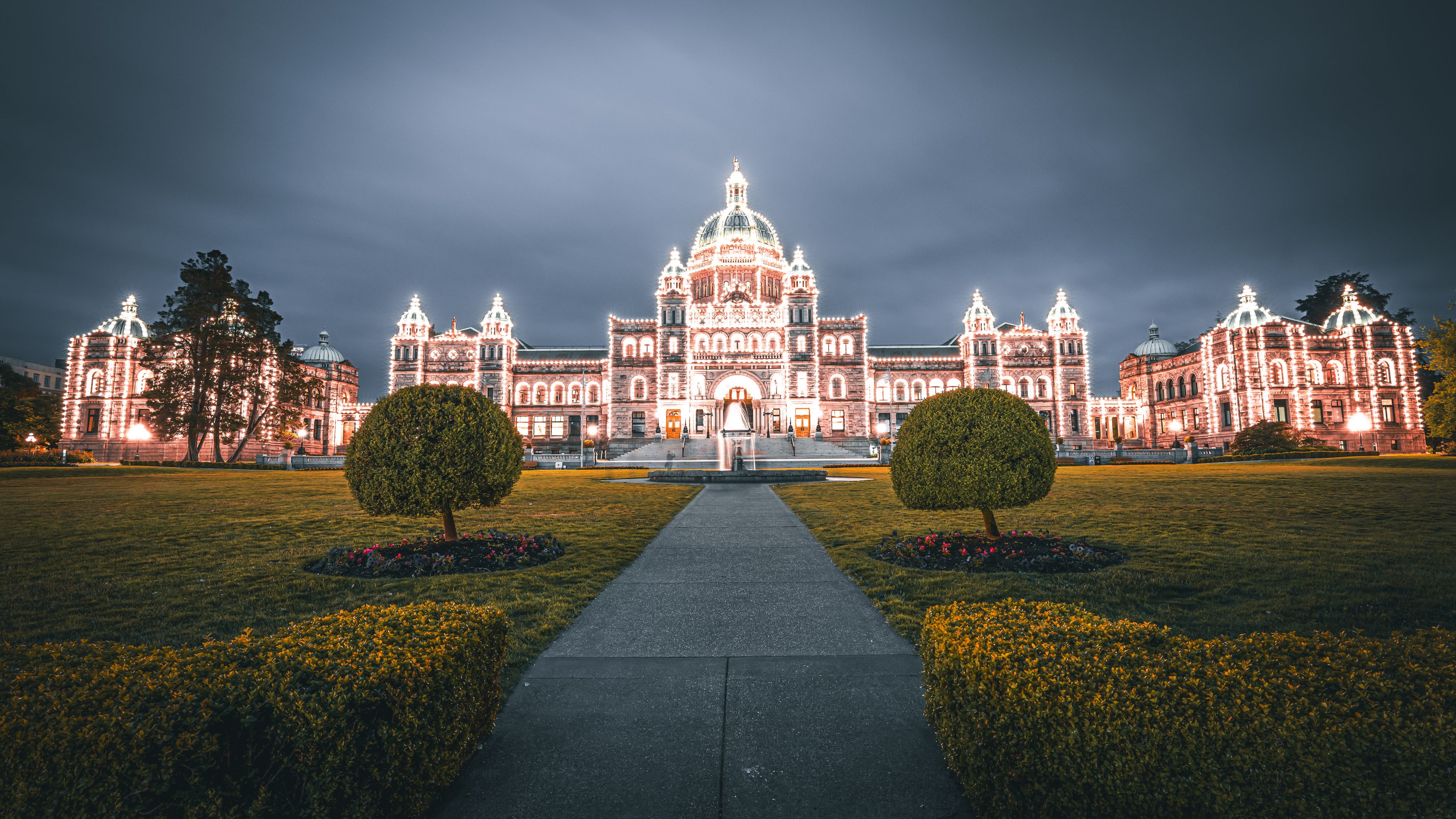 A grand illuminated building with a central dome, flanked by two symmetrical trees and a central water feature.