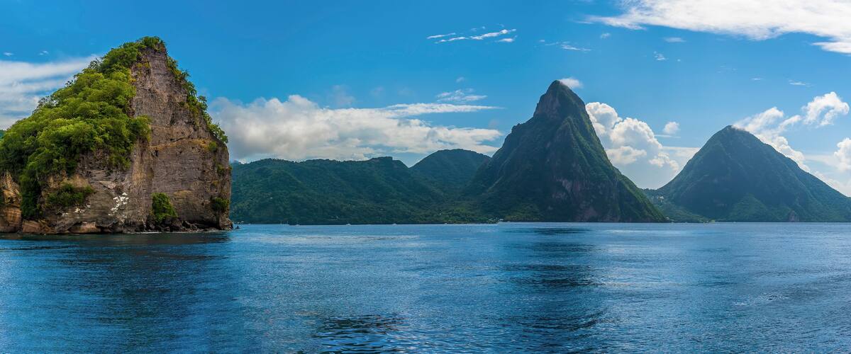 A coastal landscape with a prominent rocky island and two large mountains in the background.