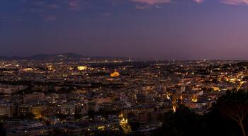 Un paisaje urbano al atardecer con edificios iluminados y una estructura en forma de cúpula destacada a lo lejos.