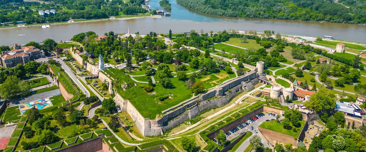 Aerial view of Belgrade where the Sava and Danube rivers meet. Visible landmarks include Kalemegdan Fortress (Beogradska tvrđava), city bridges, and Ušće Park — a perfect urban-meets-nature panorama