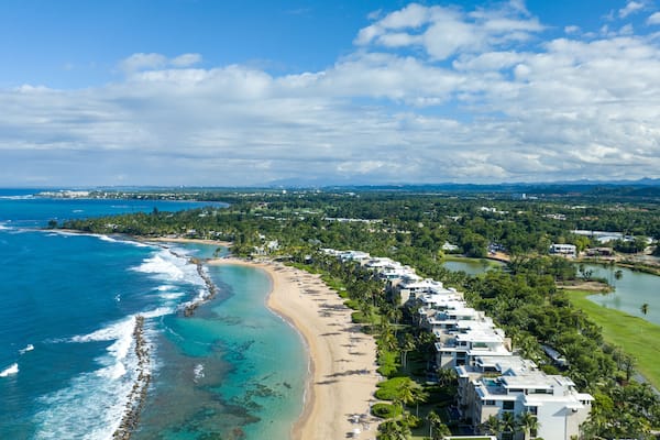An aerial view of west beach residences Dorado Beach Resort in Puerto Rico, capturing both the coastline and the adjacent golf course. To the left, the coastline runs along the blue waters.