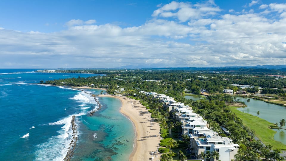 An aerial view of west beach residences Dorado Beach Resort in Puerto Rico, capturing both the coastline and the adjacent golf course. To the left, the coastline runs along the blue waters.