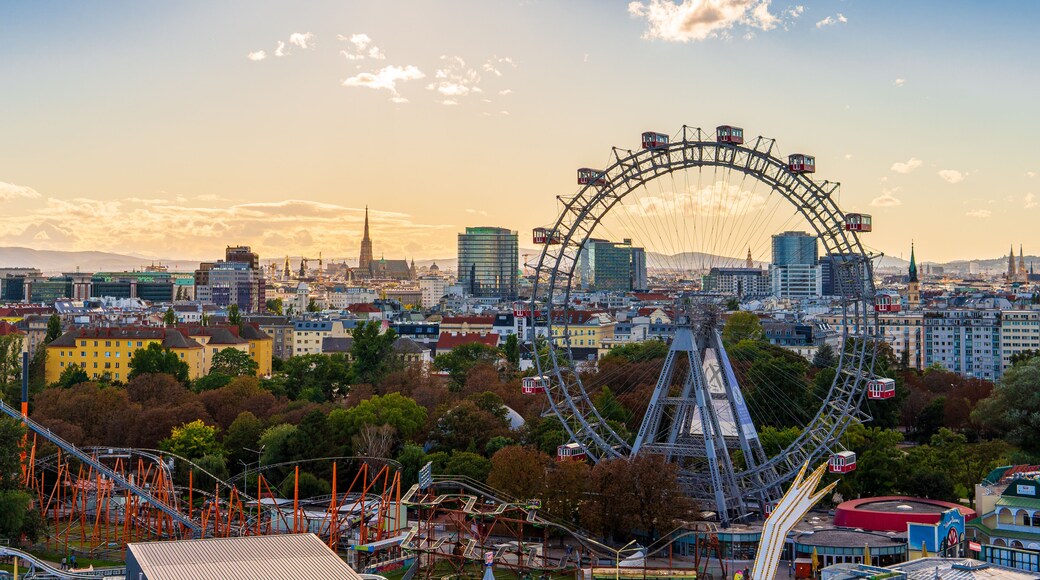 City view of Vienna, Austria, from above at Prater amusement park. Iconic fairy wheel and other amusement rides in the background with the sun peeking out of the clouds.
