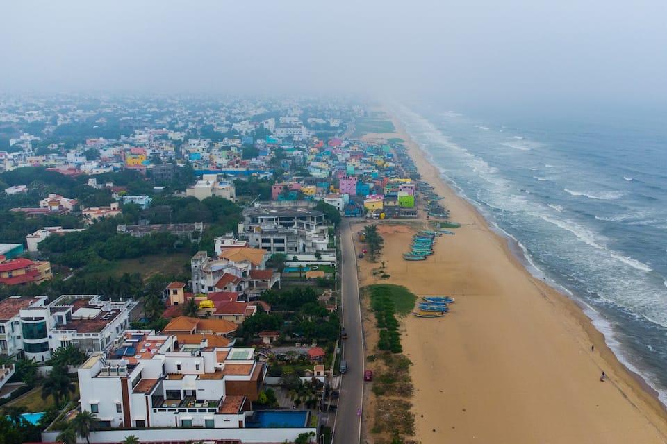 A coastal cityscape with a sandy beach, colorful buildings, and a road running parallel to the shore.