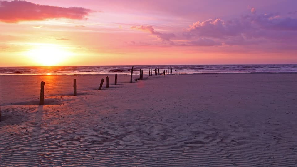 A beach at sunset with a wooden fence and ocean waves.
