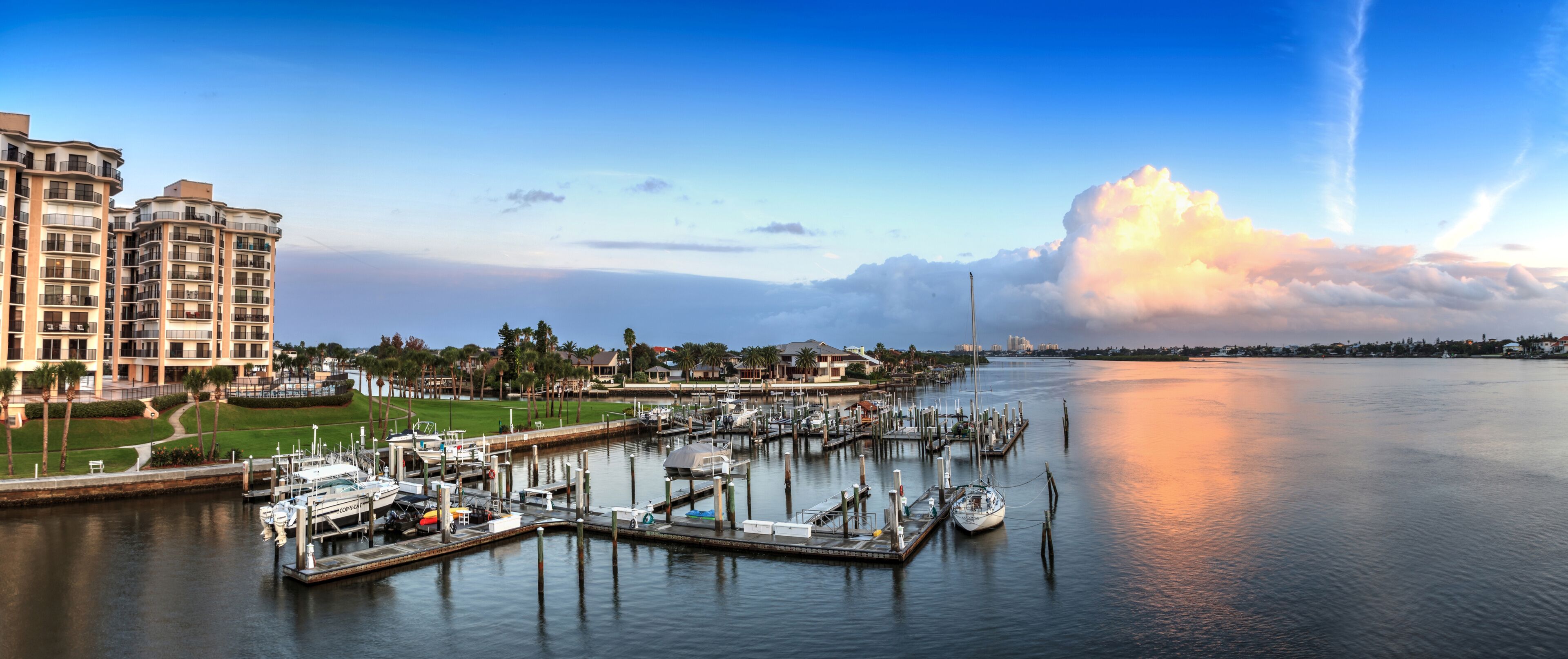 A marina with boats docked, a large building on the left, and a city skyline in the background.