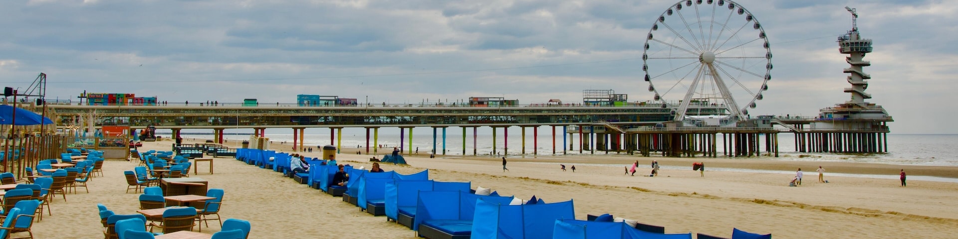 Cafe terrace on the Scheveningen beach with no consumer. There is a pier with a huge ferris wheel and a tower on it in the background