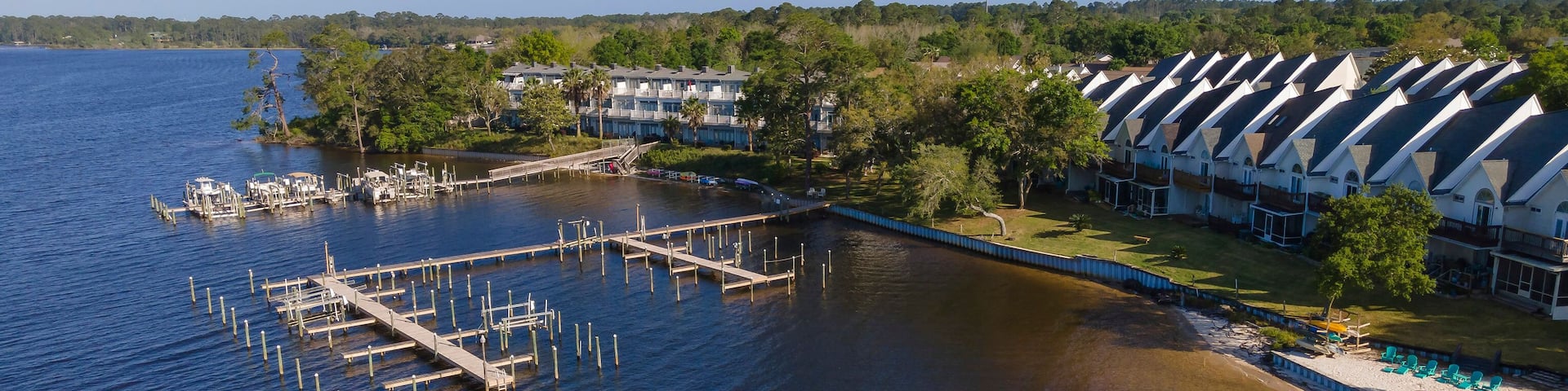 Townhouses with balconies facing the waterfront with docks in Navarre, Florida. Boat lifts and dock piles on a wooden pier at the waterfront of residential area against the sky in an aerial shot view.